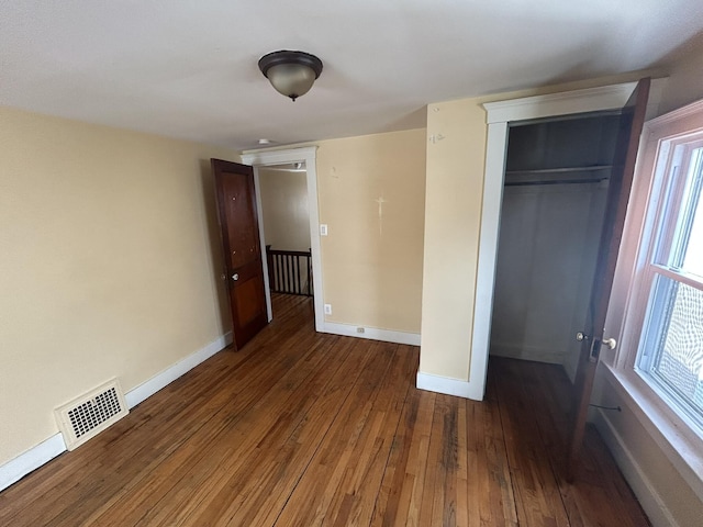 unfurnished bedroom featuring hardwood / wood-style flooring, a closet, visible vents, and baseboards