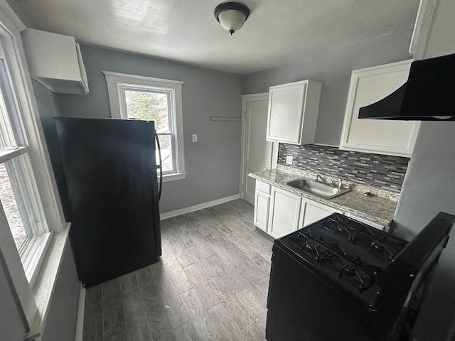 kitchen featuring light wood finished floors, tasteful backsplash, a sink, black appliances, and exhaust hood