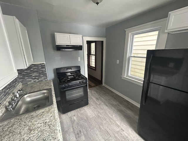 kitchen with light wood-style flooring, under cabinet range hood, black appliances, white cabinetry, and a sink