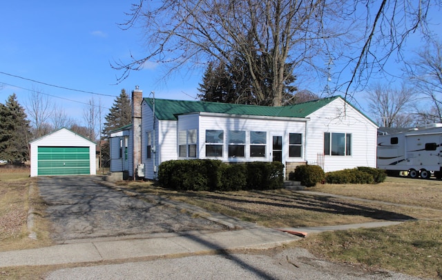 view of front of home with a chimney, a detached garage, metal roof, an outdoor structure, and a front yard