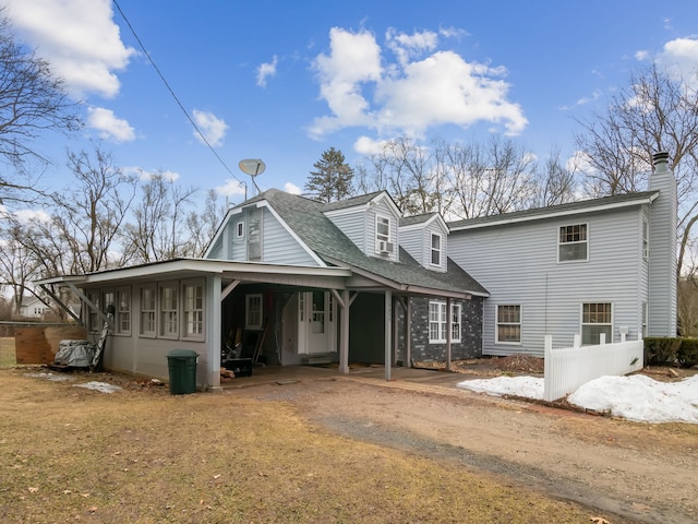 view of front of home with dirt driveway, roof with shingles, and a chimney