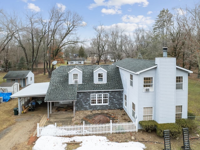 view of front of house featuring a fenced front yard, an outbuilding, an attached carport, and roof with shingles