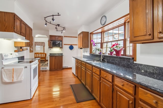 kitchen with white appliances, light wood finished floors, brown cabinetry, under cabinet range hood, and a sink