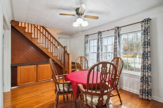 dining space featuring light wood-style floors, baseboards, stairway, and ceiling fan