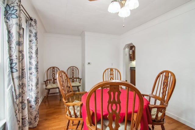 dining area with arched walkways, crown molding, a ceiling fan, wood finished floors, and baseboards