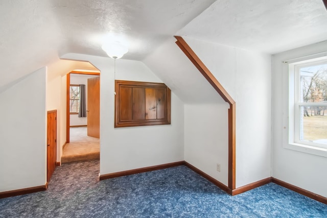 additional living space with lofted ceiling, dark carpet, and baseboards