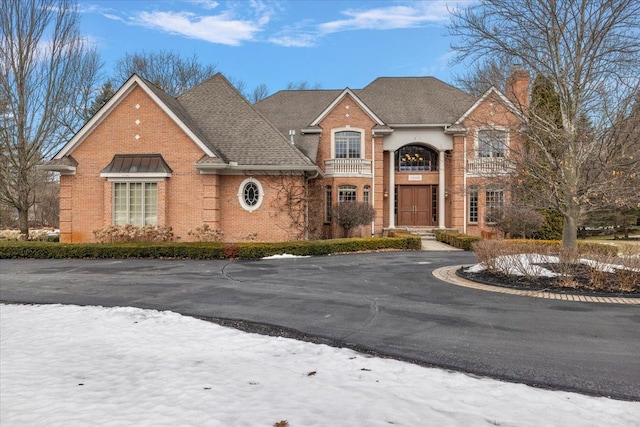 view of front of property with driveway, brick siding, a chimney, and a shingled roof