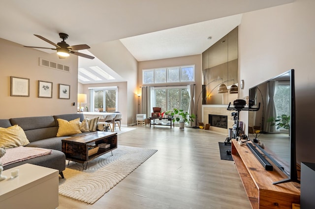 living room with a high ceiling, light wood-style floors, a fireplace, and visible vents