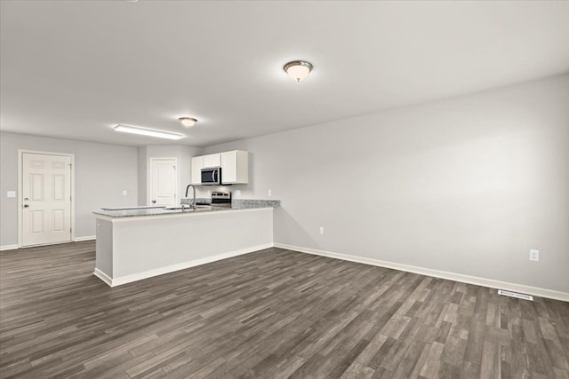 kitchen featuring dark wood finished floors, stainless steel appliances, white cabinets, a sink, and baseboards