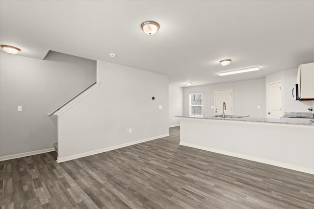 unfurnished living room featuring a sink, dark wood finished floors, and baseboards