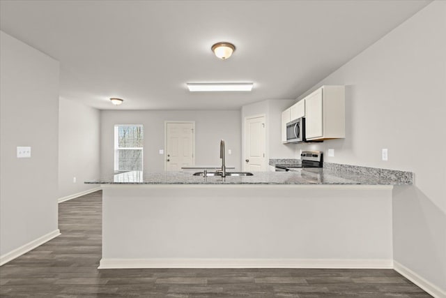 kitchen with light stone counters, appliances with stainless steel finishes, white cabinets, a sink, and a peninsula