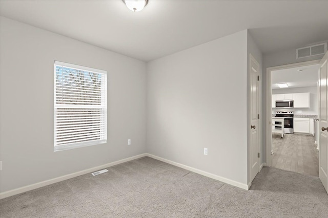 spare room featuring baseboards, visible vents, and light colored carpet