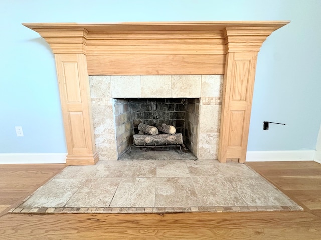 interior details with a tiled fireplace, wood finished floors, and baseboards