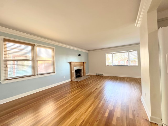 unfurnished living room featuring a fireplace with flush hearth, visible vents, baseboards, light wood-style floors, and crown molding