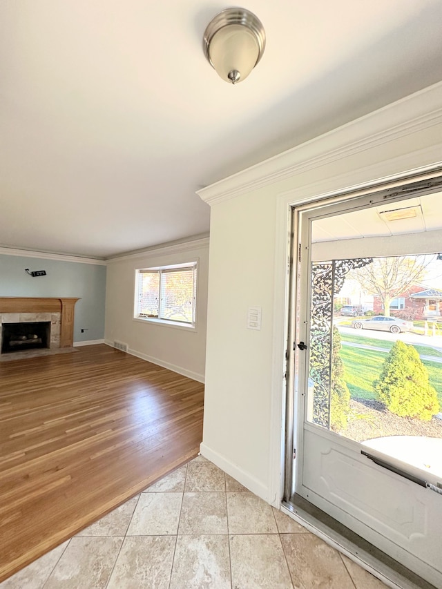 interior space with light tile patterned floors, a fireplace with flush hearth, visible vents, baseboards, and crown molding