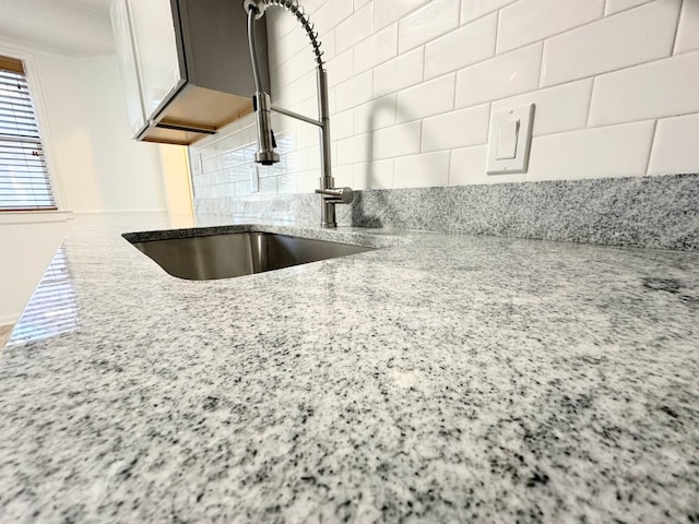 interior details with white cabinetry, tasteful backsplash, light stone counters, and a sink