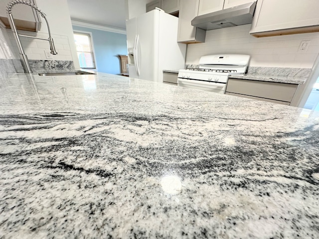 kitchen featuring white appliances, crown molding, under cabinet range hood, and light stone countertops