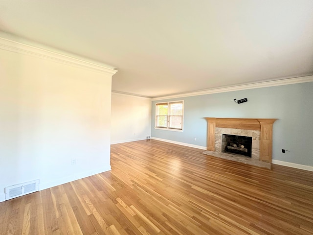 unfurnished living room with baseboards, visible vents, wood finished floors, crown molding, and a high end fireplace