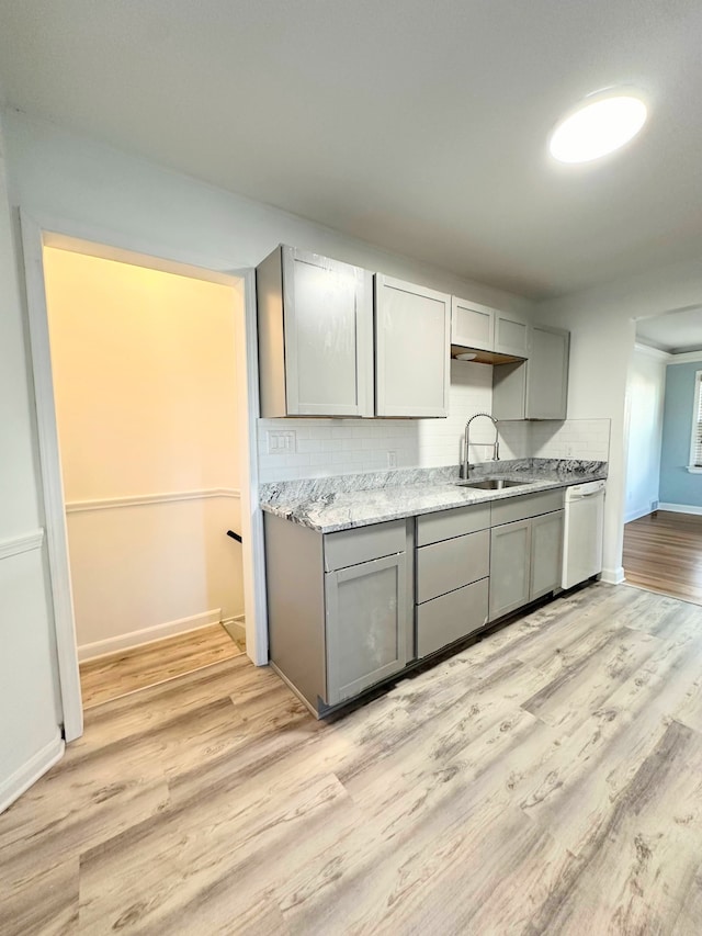 kitchen with light wood finished floors, backsplash, gray cabinetry, white dishwasher, and a sink