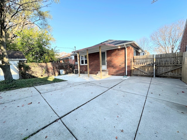 rear view of property featuring entry steps, a patio, a gate, fence, and brick siding