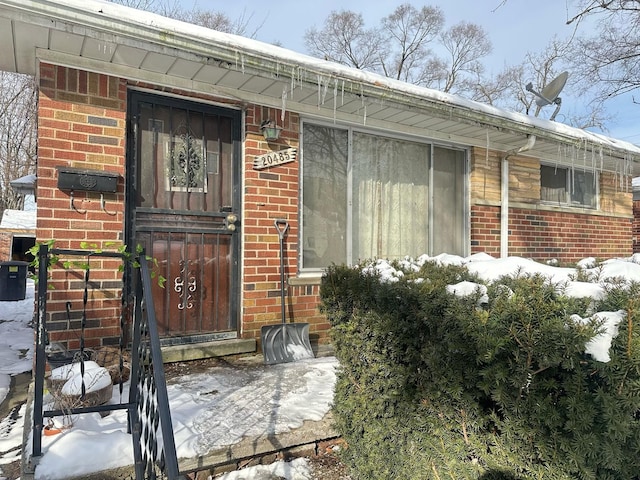 snow covered property entrance featuring brick siding