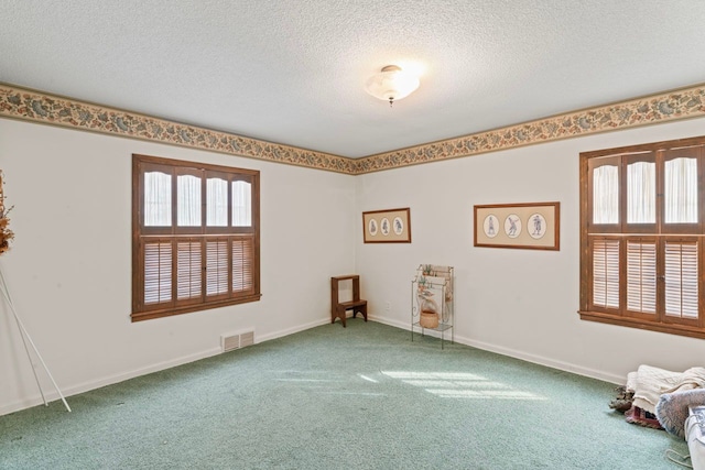 carpeted empty room with baseboards, a textured ceiling, visible vents, and a wealth of natural light