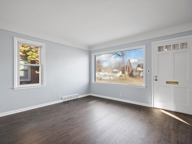 empty room featuring dark wood finished floors, visible vents, and baseboards