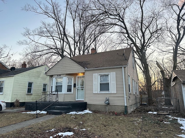 view of front of property with a shingled roof, a chimney, and fence