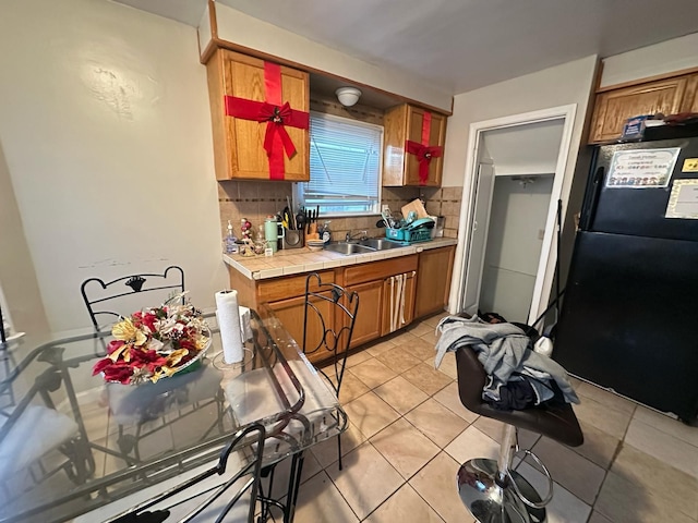 kitchen featuring tile countertops, light tile patterned floors, backsplash, freestanding refrigerator, and a sink