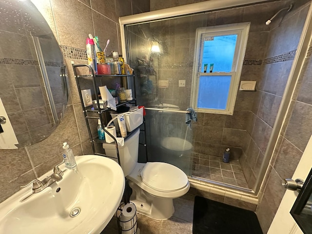 bathroom featuring a stall shower, decorative backsplash, toilet, a sink, and tile walls