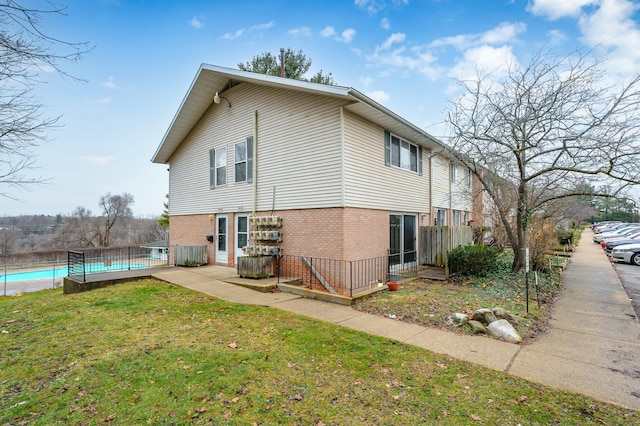 back of house featuring a fenced in pool, brick siding, a yard, and fence