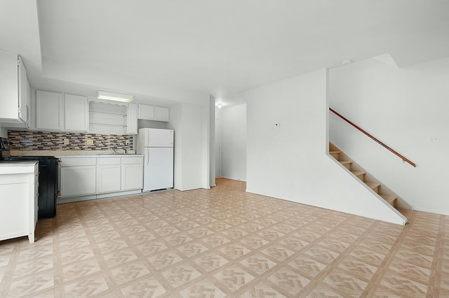 kitchen with black electric range oven, freestanding refrigerator, light countertops, light floors, and backsplash