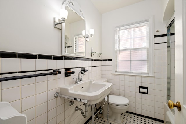 bathroom featuring a wainscoted wall, tile walls, toilet, a sink, and tile patterned flooring