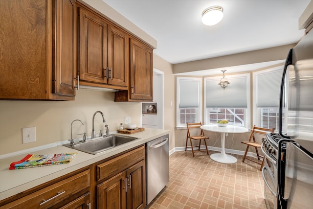 kitchen with a sink, baseboards, light countertops, appliances with stainless steel finishes, and brown cabinets