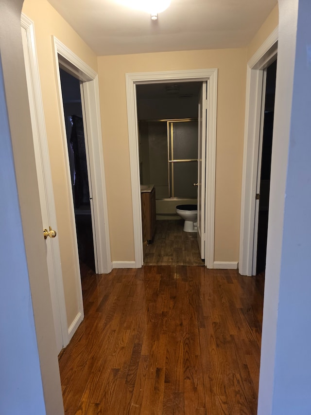 corridor featuring baseboards and dark wood-type flooring