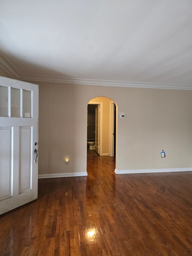 empty room with baseboards, crown molding, arched walkways, and wood finished floors