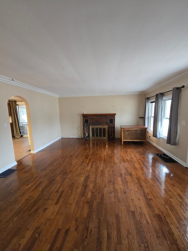 unfurnished living room with arched walkways, ornamental molding, a brick fireplace, and dark wood-style floors