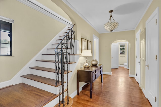 foyer with arched walkways, wood finished floors, baseboards, stairs, and ornamental molding