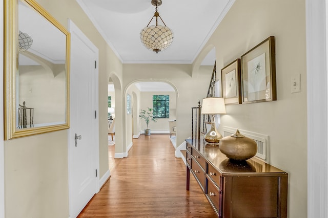 hallway featuring ornamental molding, arched walkways, baseboards, and wood finished floors