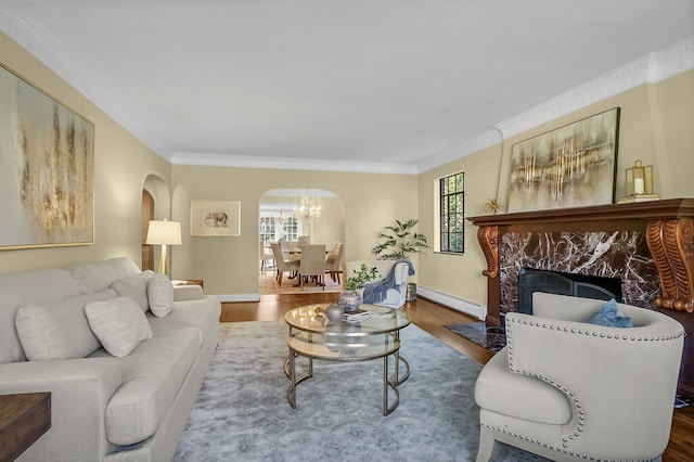 living area with arched walkways, wood finished floors, baseboard heating, crown molding, and a high end fireplace