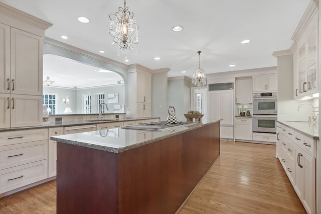 kitchen with light wood finished floors, double oven, crown molding, and a sink