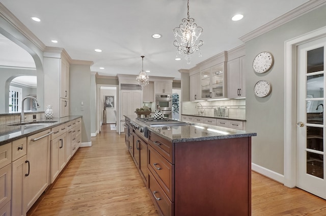 kitchen with arched walkways, a sink, appliances with stainless steel finishes, ornamental molding, and a center island