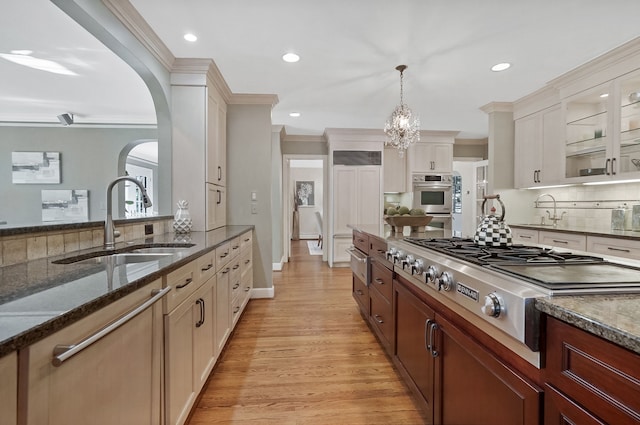 kitchen featuring decorative backsplash, appliances with stainless steel finishes, ornamental molding, dark stone countertops, and a sink