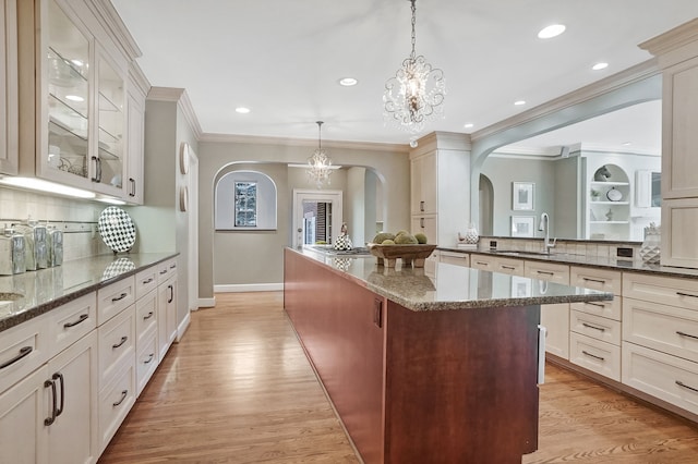 kitchen featuring arched walkways, dark stone counters, light wood-style flooring, a kitchen island, and a sink