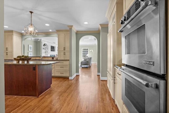 kitchen with arched walkways, ornamental molding, hanging light fixtures, stainless steel double oven, and light wood-type flooring