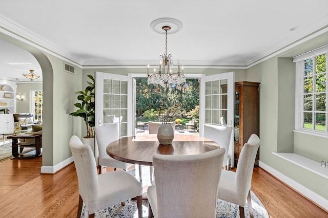 dining space featuring crown molding, a chandelier, arched walkways, and wood finished floors