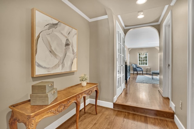 corridor with arched walkways, french doors, crown molding, wood finished floors, and baseboards