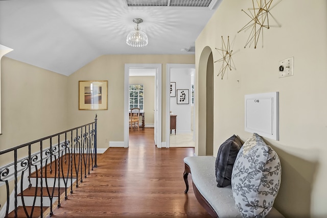 corridor with baseboards, arched walkways, wood finished floors, vaulted ceiling, and an upstairs landing