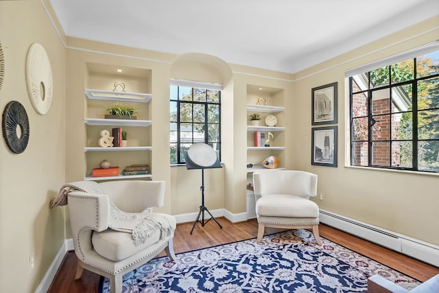 sitting room featuring built in features, a baseboard radiator, baseboards, and wood finished floors