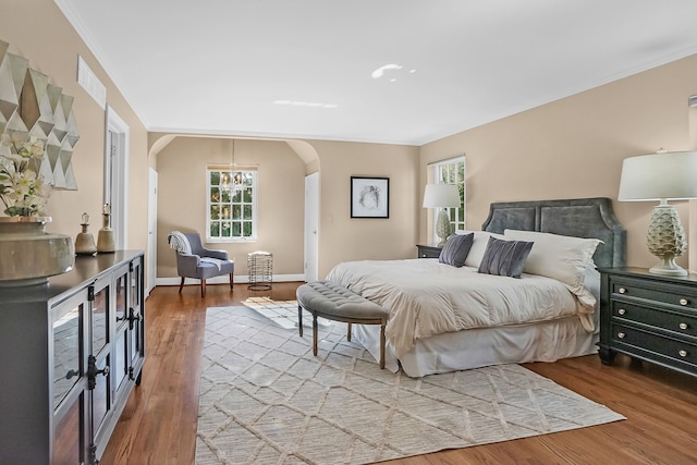 bedroom featuring arched walkways, ornamental molding, wood finished floors, and baseboards